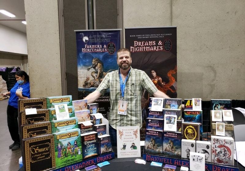 Maxwell Alexander Drake at his convention booth with the books he has written